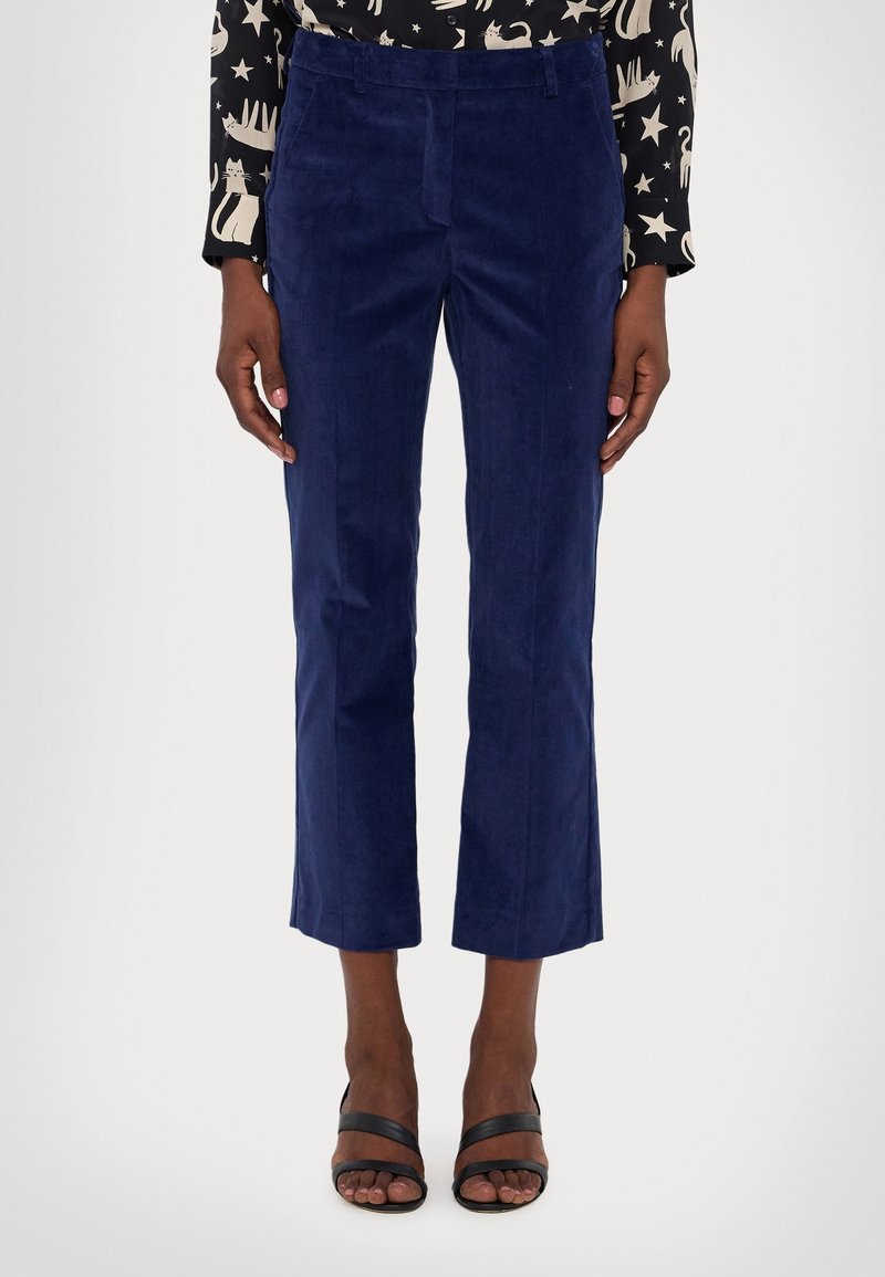 Pantalon court en velours côtelé bleu marine avec une coupe droite, présentant une texture subtile à côtes et des poches latérales. Porté avec des sandales noires à lanières.