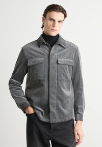 Gray striped corduroy shirt with a collar, two chest pockets, and button closure. It has long sleeves and a relaxed fit design.