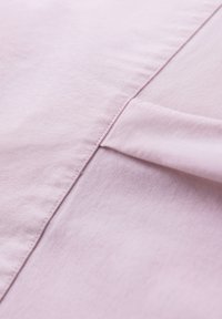Gros plan d'une couture en tissu rose clair avec un petit détail de tissu plié le long de la ligne de couture.