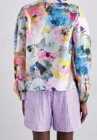 Multicolored floral-patterned long-sleeve top with a shiny texture, paired with lavender pleated shorts featuring subtle vertical stripes.