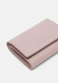 Portafoglio in pelle rosa chiaro con una texture liscia, caratterizzato da un design pieghevole e un logo del marchio impresso sul davanti. Cuciture in ordine come dettaglio.
