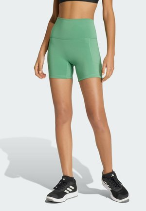 Jasnozielone szorty z wysokim stanem wykonane z elastycznego materiału o gładkiej fakturze, z bocznymi kieszeniami i dopasowanym krojem. Ubrane z czarnymi trampkami.