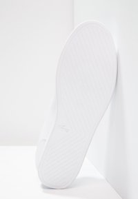 Bílá podešev tenisky s texturovaným vzorem pro lepší přilnavost a minimalistickým designem, se subtilním vyraženým logem na boku.