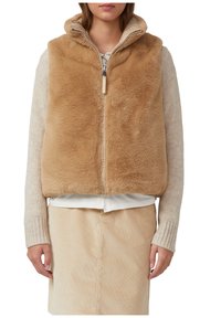 Bruine nepbont vest met een capuchon en ritsluiting, gecombineerd met een crèmekleurig langmouwtop en een beige corduroy rok. Zacht, gestructureerd materiaal.