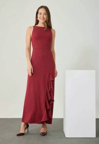 Vynio margo be rankovių suknelė su prigludusiu bodi ir raukiniais apatinėje dalyje. Lygus audinys, ilgas iki žemės, derinamas su tamsiomis aukštakulnėmis bateliais.