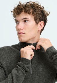 Mørkegrå zip-neck genser med ribbestrikket mansjetter og krage. Myk tekstur, slim fit, med en halv glidelås i nakken for justerbar dekning.