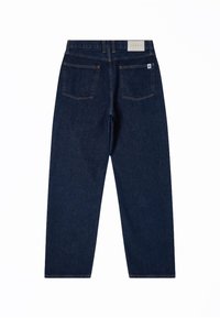 Jean en denim bleu foncé vu de dos avec deux grandes poches arrière et une petite étiquette blanche sur la poche droite.