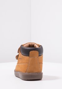 Wasserdichte braune Wildleder-Ankle-Boots mit schwarzen Lederakzenten, runder Ferse und Klettverschluss. Sichtbare Steppnähte.
