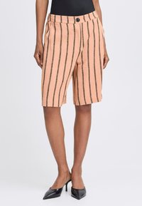 Shorts pêche clair à rayures verticales noires, avec une coupe ajustée, un bouton à l'avant et des poches sur les côtés. Tissu lisse avec une texture subtile.