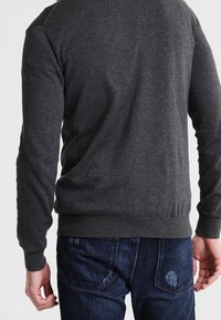 Szara dzianinowa bluza z długimi rękawami, ściągaczami na mankietach i dole, noszona z niebieskimi jeansami, prezentująca prosty, czysty design.