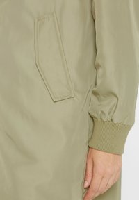 Leichte olivgrüne Bomberjacke mit Seitentasche, gerippten Bündchen und glatter, glänzender Stoffoberfläche. Legere und funktionale Designdetails.