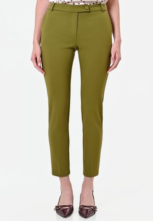 Pantaloni aderenti verde oliva alla caviglia, chiusi con un bottone, indossati con tacchi a punta color bordeaux e una maglietta a pois parzialmente visibile.