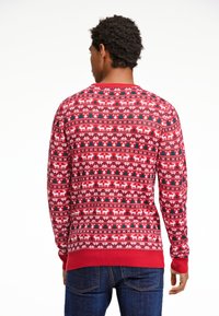 Röd tröja med vintermönster, med vita renar och gröna träd, ribbade ärmslut och nederkant, stickad textur.