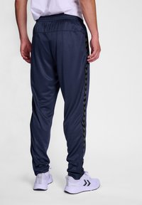 Marineblauwe sportbroek met elastische tailleband en zijstrepen met een zwart zigzagpatroon. Gemaakt van glad, ademend materiaal.