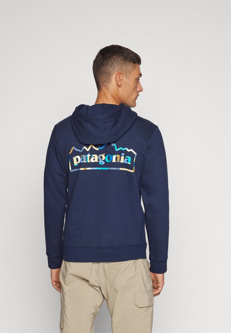 Hanorac bleu marin cu buzunar tip kenguru și glugă cu șnur. Are un logo colorat "patagonia" pe spate; textură moale și grosime medie.