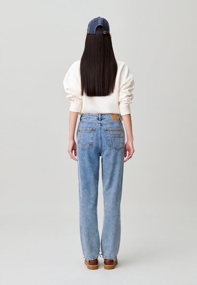 Vaqueros azul claro de talle alto con pierna recta, combinados con una sudadera cremosa y una gorra azul marino, vistos desde atrás.