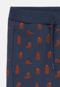 Marineblauwe katoenen joggingbroek met een herhaald patroon van bruine beren in verschillende poses. Elastische tailleband met een trekkoord.