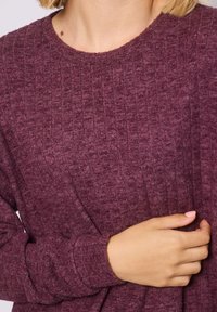 Suéter de punto acanalado burdeos con cuello redondo, tejido texturizado y mangas largas. La tela parece suave y ligeramente elástica.