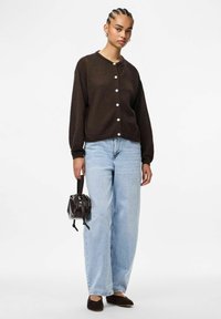 Cardigan marrón de punto con seis botones blancos, combinado con jeans de pierna ancha de color azul claro. Los accesorios incluyen un bolso pequeño marrón y zapatos oscuros.