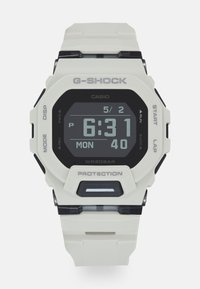 Montre numérique G-Shock avec un boîtier et un bracelet en résine blanche, un écran numérique noir et des accents gris. Dispose de boutons pour le mode et le chronomètre.