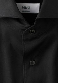 Camicia nera a maniche lunghe con tessuto liscio, dotata di colletto a punta e chiusura con un bottone. Etichetta del marchio "MNG" visibile.