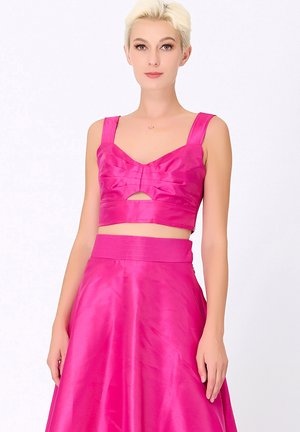 Ensemble deux pièces fuchsia comprenant un haut court avec un détail en nœud et des bretelles larges, associé à une jupe fluide taille haute. Texture lisse.