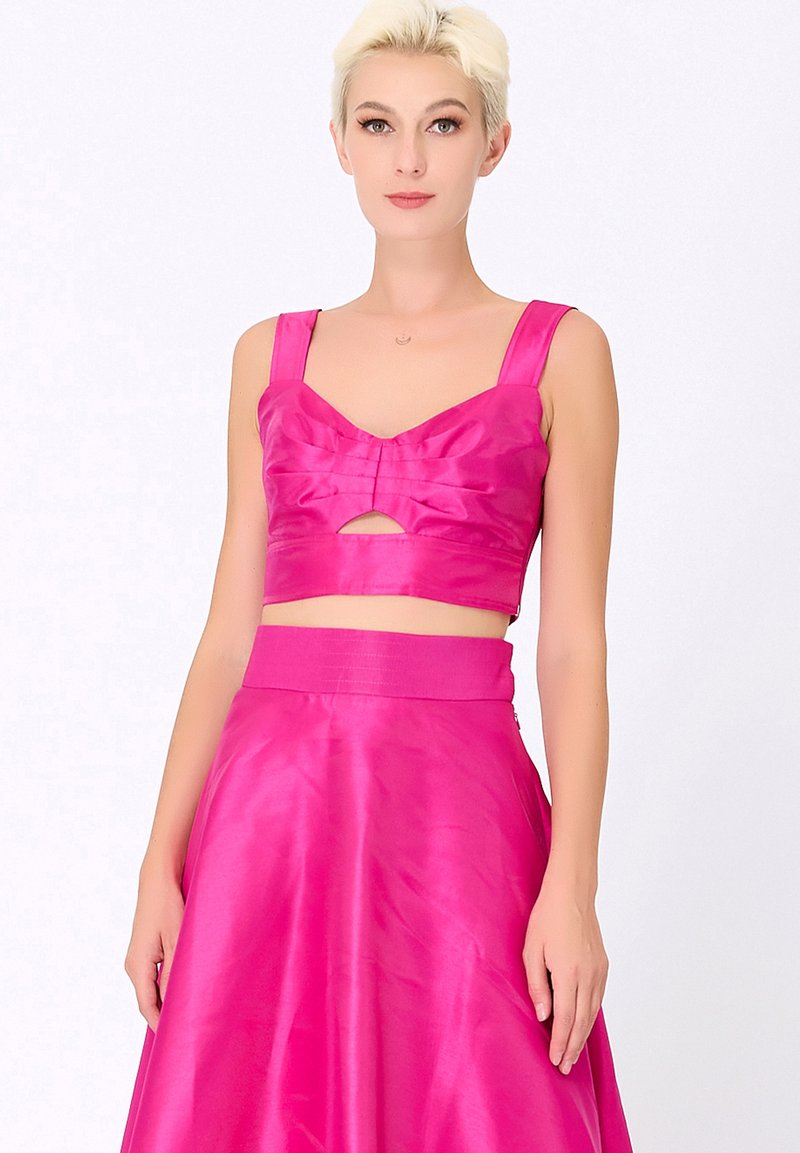 Ensemble deux pièces fuchsia comprenant un haut court avec un détail en nœud et des bretelles larges, associé à une jupe fluide taille haute. Texture lisse.