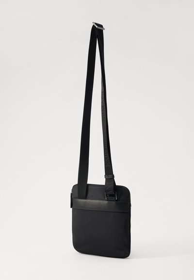 Borsa a tracolla nera in nylon liscia con un'accoppiatura in pelle, dotata di una lunga tracolla regolabile e chiusura con cerniera. Forma rettangolare compatta.