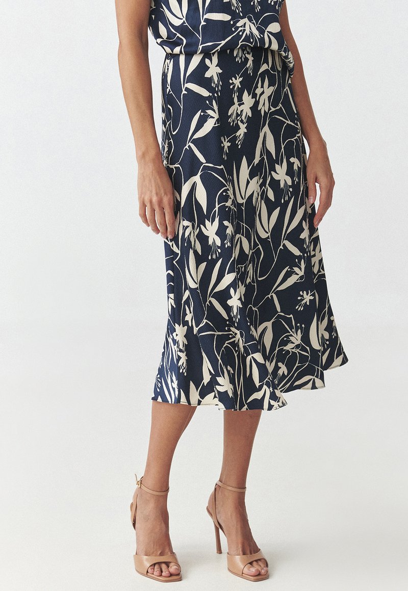 Navy blue skirt with white floral patterns, knee-length, flowing design. Pair of nude high-heeled sandals complements the outfit.