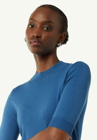 Niebieski dziergany sweter o dopasowanym kroju, okrągłym dekolcie i krótkich rękawach z prążkowanymi mankietami. Miękka faktura i gładkie wykończenie.