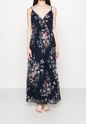 Marineblauwe maxi-jurk met bloemenprint, dunne bandjes, overslagontwerp en elastische taille. Voorzien van verschillende kleurrijke bloemen op een doorschijnende stof.
