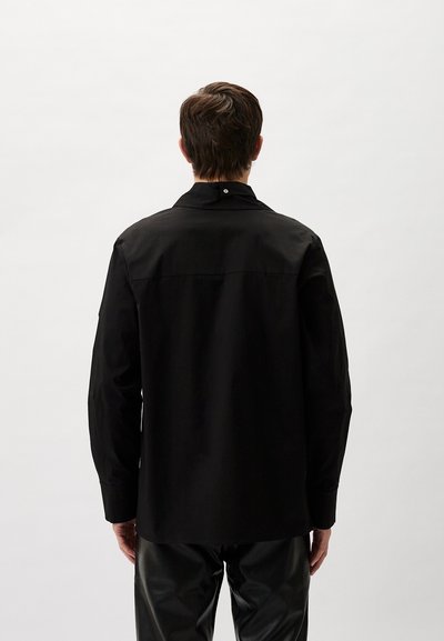 Schwarz langärmliges Hemd mit spitzem Kragen, aus glattem Stoff gefertigt. Verfügt über einen einzelnen Knopf am Hals und ein gerades Rückendesign.