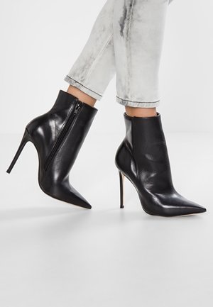 Stivaletti in pelle nera con punta e tacco a spillo alto indossati con jeans grigio chiaro risvoltati, con dettaglio della cerniera laterale.