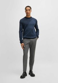 Maglione in maglia blu navy con texture diagonale, abbinato a pantaloni grigi chiari su misura e stivaletti neri alla caviglia. Design semplice con collo a giro, stile aderente.