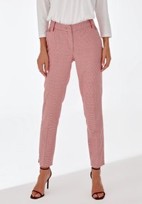 Pantalons slim-fit à carreaux rouges et blancs avec fente latérale, dotés d'une taille standard et de poches avant. Portés avec des talons noirs à lanières.