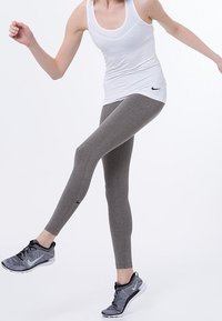 Leggings de sport gris en tissu extensible, associés à un débardeur blanc ajusté et des chaussures de course noires et blanches.