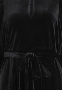 Svart sammetklänning med en mjuk textur, löst liv och ett knytbälte i midjan som skapar en skräddarsydd silhuett.