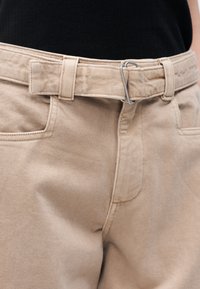 Μπεζ παντελόνι με ταιριαστή υφασμάτινη ζώνη που ασφαλίζεται με ασημένια μεταλλική πόρπη, φορεμένο με μαύρο ριμπ τοπ που έχει μαζευτεί μέσα.