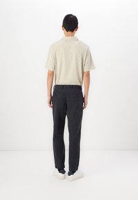 Polo bej cu mânecă scurtă, cu un model texturat în carouri, asociat cu pantaloni gri închis și sneakers albi. Design simplu, croi ajustat.