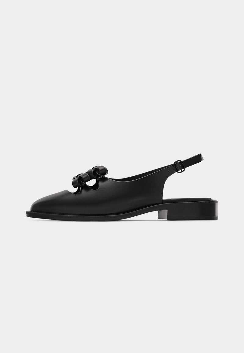 Black leather flat slingback shoe with low heel and three decorative bows on the upper, side view on white background.