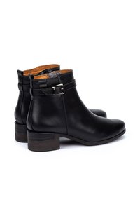 Botas negras de cuero hasta el tobillo con un tacón bajo y apilado, que presentan un detalle de hebilla y un forro texturizado marrón. Exterior liso con costuras mínimas.