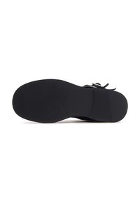 Suela de zapato negra con superficie texturizada, diseñada para ofrecer agarre. Presenta una ligera curva en la puntera y un tacón plano para mayor estabilidad.