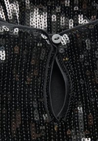 Musta paljettikangas, jossa on ympyrämuotoisia paljetteja peittämässä pinnan, keskeisellä napilla suljettava, avonainen kaula-aukko, joka johtaa kiinteään mustaan vuoriin.