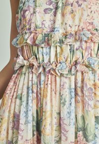 Abito a stampa floreale realizzato in tessuto leggero, con dettagli arricciati sul busto e in vita, in colori pastello come rosa, viola e verde.