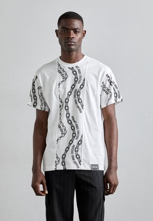 T-shirt en coton blanc avec des motifs de chaînes et de texte noirs sur le devant, à manches courtes, et une étiquette de marque à l'ourlet.