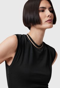 Svart ärmlös topp med en slät textur, som har en smal guldig detalj runt halsringningen och en figurnära design.