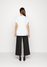 Top bianco a maniche corte con vestibilità rilassata, abbinato a pantaloni neri a gamba larga e sandali neri con tacco. Colore uniforme senza motivi visibili.