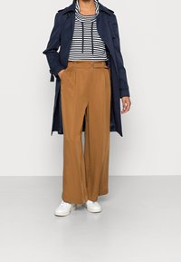 Námořnický trenčkot přes černobílý pruhovaný svetr, doplněný širokými béžovými kalhotami a bílými teniskami. Má opasek a kapsy.