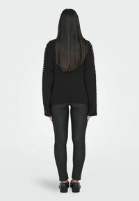 Maglione nero a coste con maniche ampie, caratterizzato da dettagli laterali, abbinato a pantaloni neri aderenti e scarpe nere. Modello di spalle.