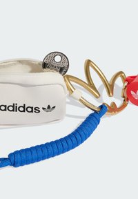 Biała saszetka z czarnym logo „adidas”; złote okucia w kształcie liścia; niebieski sznurek; srebrny brelok z fakturowaną powierzchnią. Czerwona metka z logo.